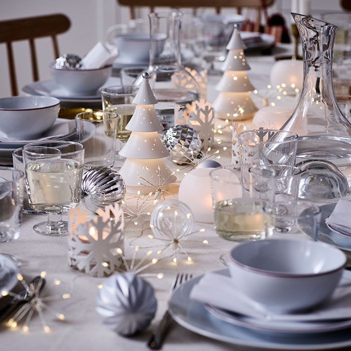 VINTERFINT decorations and STRÅLA lighting are on a festively decorated dinner table in tones of white and silver.