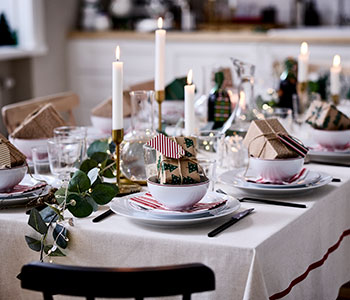 A cosy Christmas table is set with VINTERFINT decorations, lit candles and small wrapped presents in bowls.