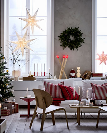 A cosy living room with tall windows is decorated for Christmas with VINTERFINT decorations and STRÅLA lighting