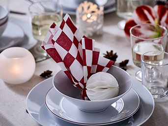 A red and white-checkered VINTERFINT paper napkin is playfully folded and set in a bowl, on a Christmas dinner table.
