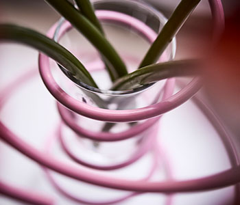 A closeup of a pink VINTERFINT vase highlights the playful curved steel and glass materials.