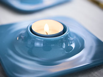 One light blue VINTERFINT tealight holders have lit tealights in them, both are on a table