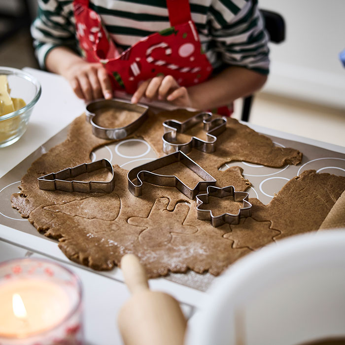 A child is using VINTERFINT pastry cutters to make festive cookie shapes from a flattened gingerbread dough.