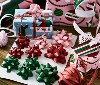 A set of VINTERFINT gift bows in green, red and pink is surrounded by ribbons and wrapped presents and gift wrappers.