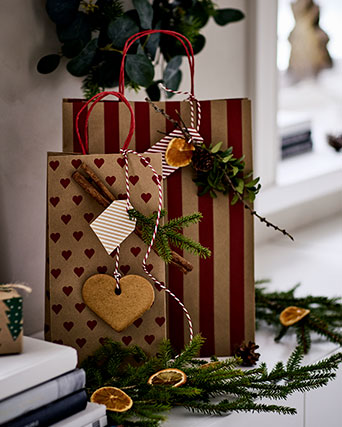 Two VINTERFINT gift bags, one with a heart pattern, the other with stripes, stand in a wooden box next to a small vase.