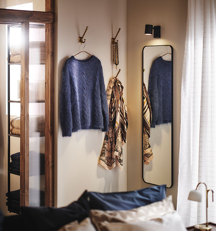 Corner of a bedroom with LINDBYN mirror and hooks for clothes and accessories on the walls. Glass doors and window at the sides.