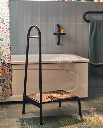 Black step stool with storage shelf placed next to bathtub in tiled bathroom
