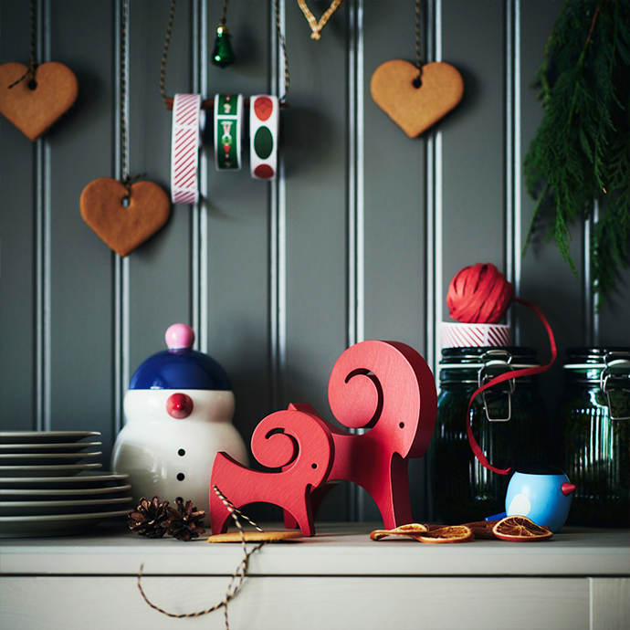 Holiday decorations on kitchen shelf with heart-shaped gingerbread cookies, red wooden reindeer ornaments, ceramic snowman jar, glass containers with festive ribbons and evergreen sprigs