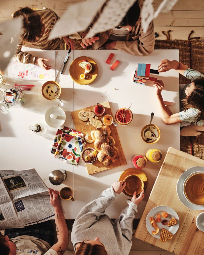 A family of five, viewed from above enjoying a leisurely breakfast around their large white dining table.
