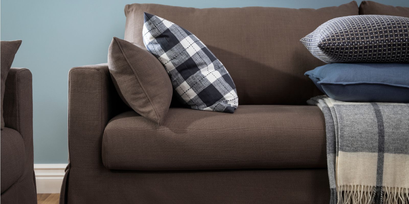 A cushion with a chequered SVAMPFLY cushion cover lies on a HYLTARP 3-seat sofa near some other cushions and a throw.