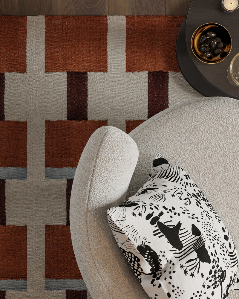 A cushion with a STOCKHOLM 2025 cushion cover lies on a STOCKHOLM 2025 armchair on a STOCKHOLM 2025 rug.