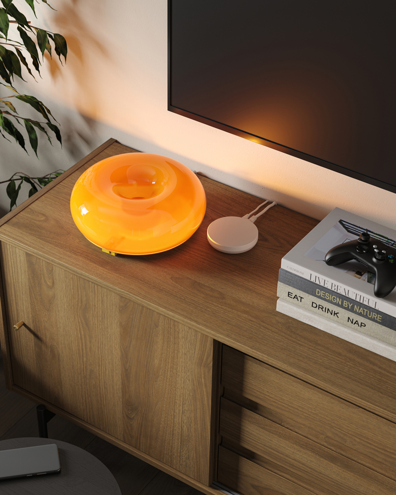 A VARMBLIXT LED table/wall lamp sits near a DIRIGERA hub and some books on a RÅDMANSJÖ TV bench underneath a wall-mounted TV.