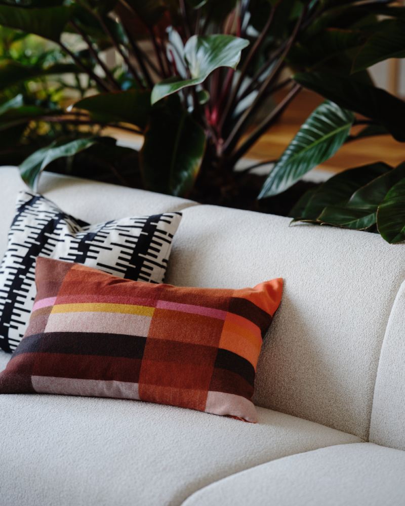 A sofa, with two cushions with different STOCKHOLM 2025 cushion covers on it, stands in front of some plants.