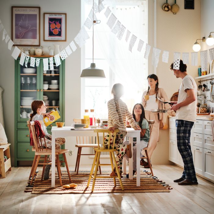A mum and dad stand in the kitchen looking at the table where their three children are sitting enjoying breakfast.