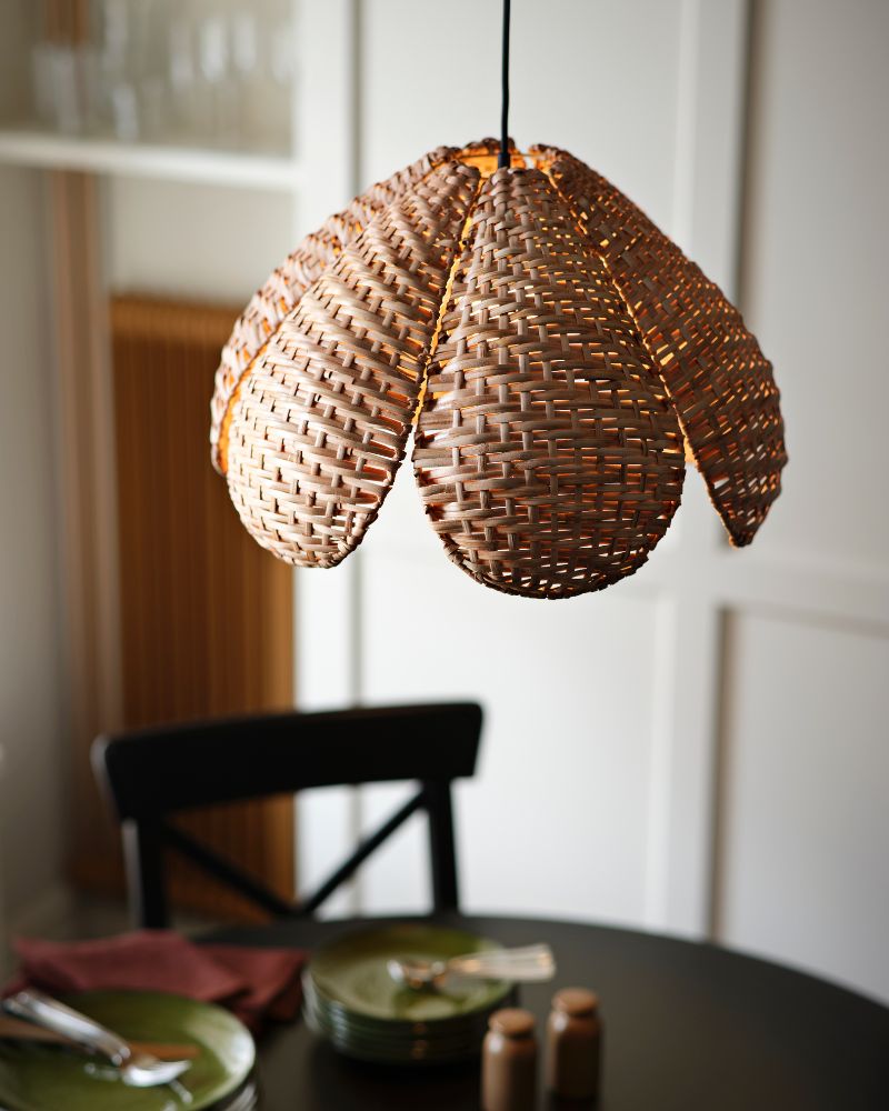 A warm-toned SANDKORN pendant lampshade featuring a woven design, hanging above a dining table with green plates.