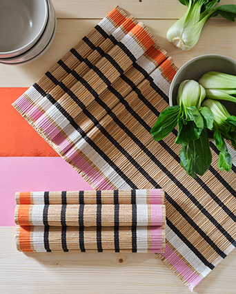 Two MÄVINN table-runners lie on a painted wooden table. The table also holds ceramic bowls and green vegetables.