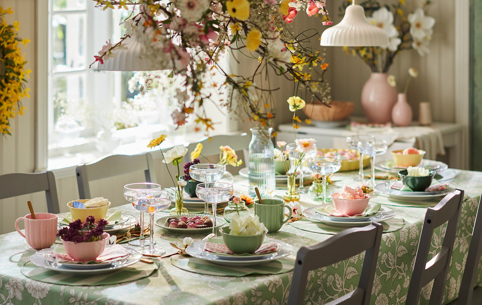 A bright dining setting featuring SMÖRFISK mugs and UPPLAGA bowls among floral decorations and elegant glassware.