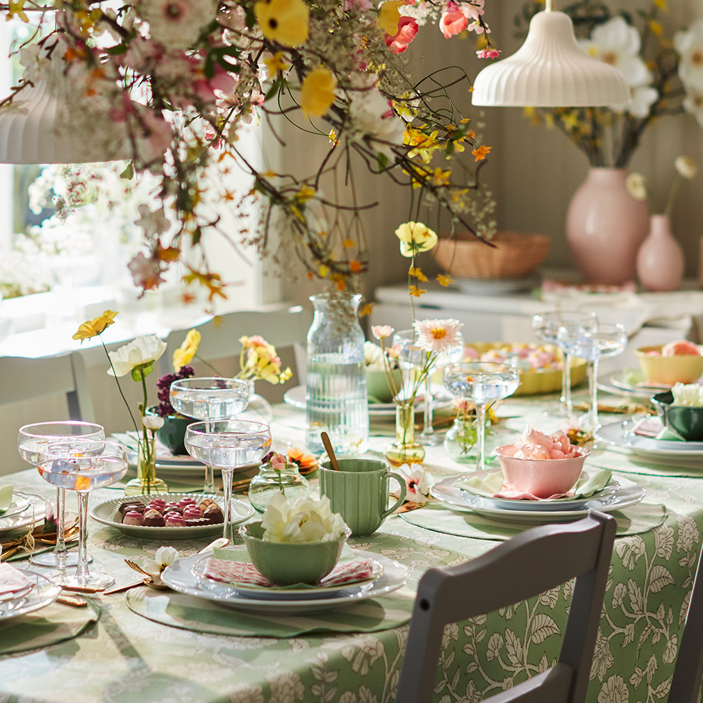 A bright dining setting featuring SMÖRFISK mugs and UPPLAGA bowls among floral decorations and elegant glassware.