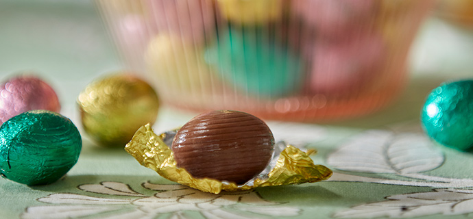 A close-up of a VÅRKÄNSLA milk chocolate egg, on top of a green, floral-patterned SMÖRFISK tablecloth.