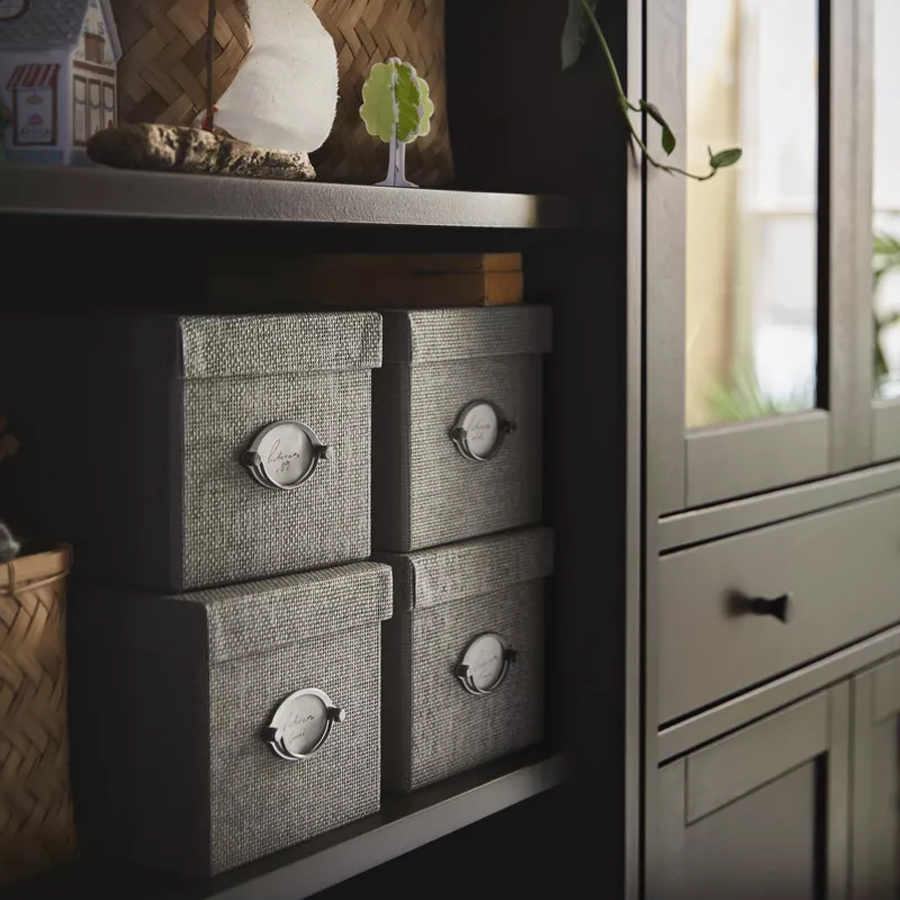 Gray fabric boxes with metal labels on a dark shelf.
