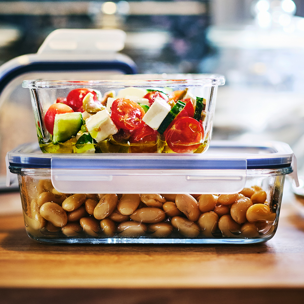 A small IKEA 365+ glass food container filled with a salad is on top of a larger IKEA 365+ container filled with beans.