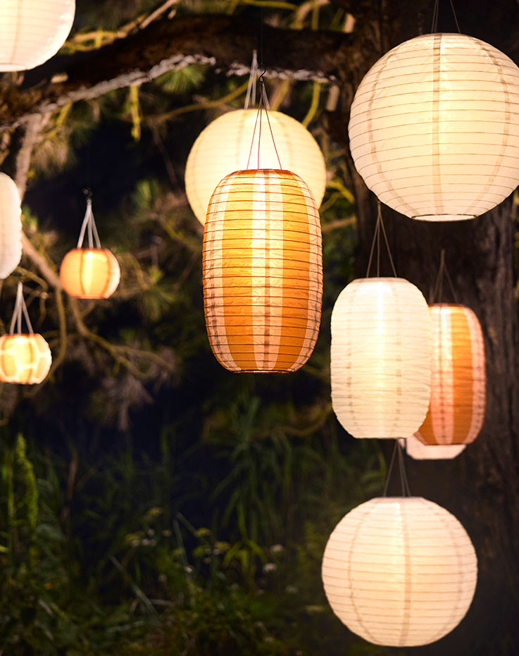An outdoor area is illuminated by many white and striped orange SOLVINDEN pendant lamps that enhances the ambiance.