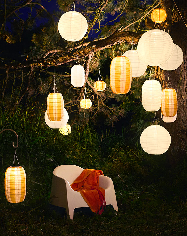 An evening garden with a white chair and plenty of hanging white and orange solar-powered SOLVINDEN pendant lamps.