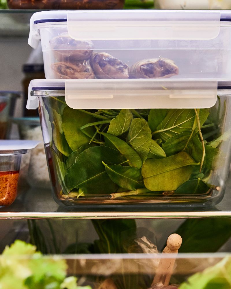 A close-up of IKEA 365+ glass food containers filled with salad and other ingredients in a refrigerator.