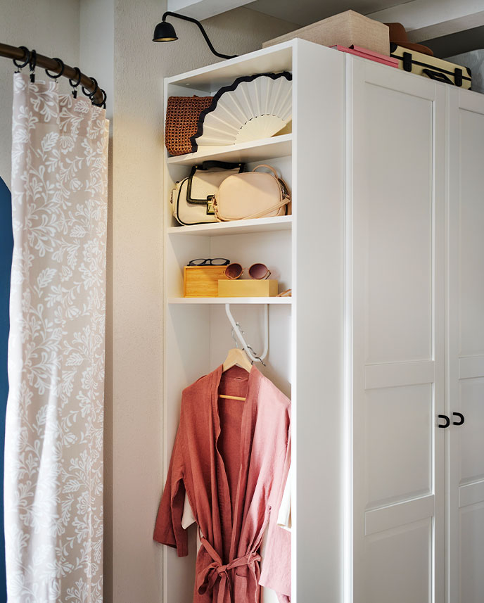 A white PAX/TYSSEDAL wardrobe combination in a bedroom with the end unit holding a dressing gown, handbags and accessories