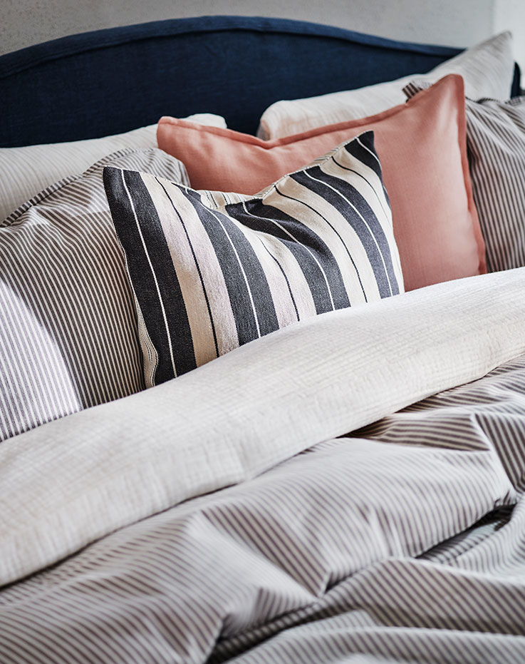 The top of a RAMNEFJÄLL bed covered in SCHERSMIN and SOLFIBBLA bed linen and cushions in LAGERPOPPEL and KORALLBUSKE covers.