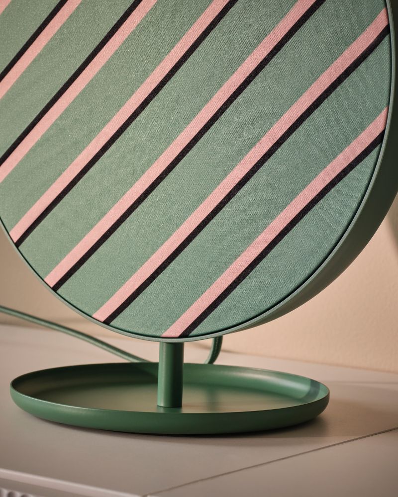 A green SOLSKYDD Bluetooth speaker with a striped design and mounted on its stand, placed on a surface by a wall.