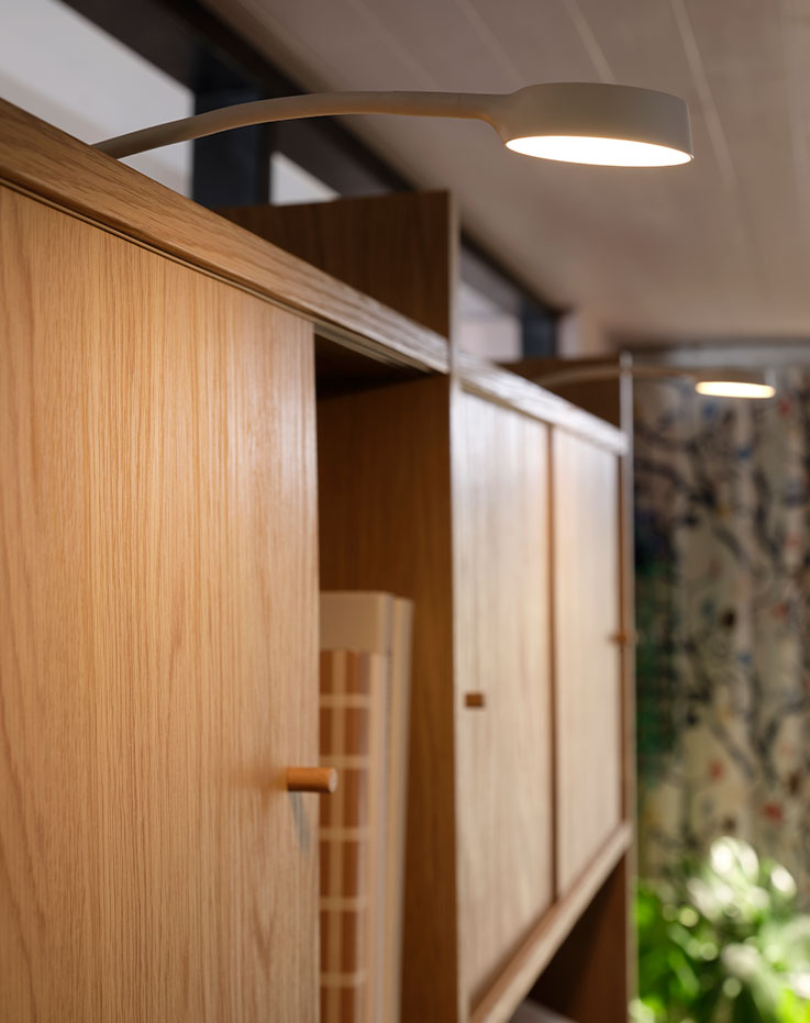 Lit YTBERG cabinet lighting mounted on top of a LÅDMAKARE storage combination with sliding doors in a light living room.