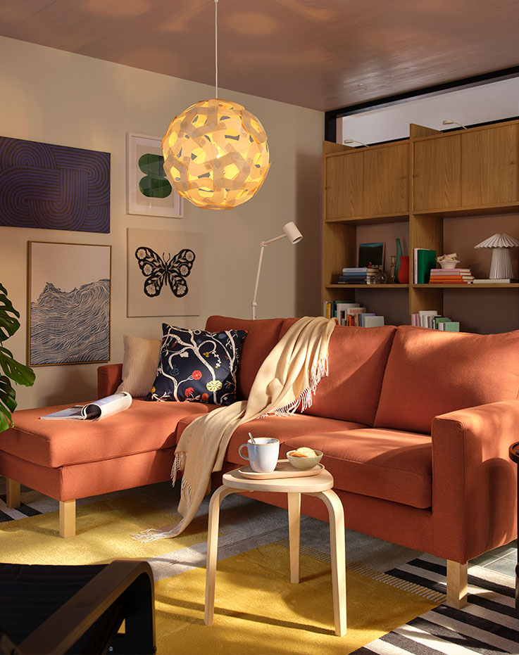 A living room with a red-brown SALTSJÖBADEN three seat sofa with chaise longue, surrounded by modern decor and plants.