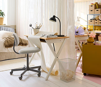 Un lado de una habitación compartida con un escritorio BOLLPOJKE en blanco/pino y una silla junto a una cama, separados por cortinas ligeras