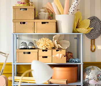 Una pared luminosa con una estantería SÅGMÄSTARE de color gris azulado claro, en la que se exponen cajas organizadas y objetos decorativos en los estantes.