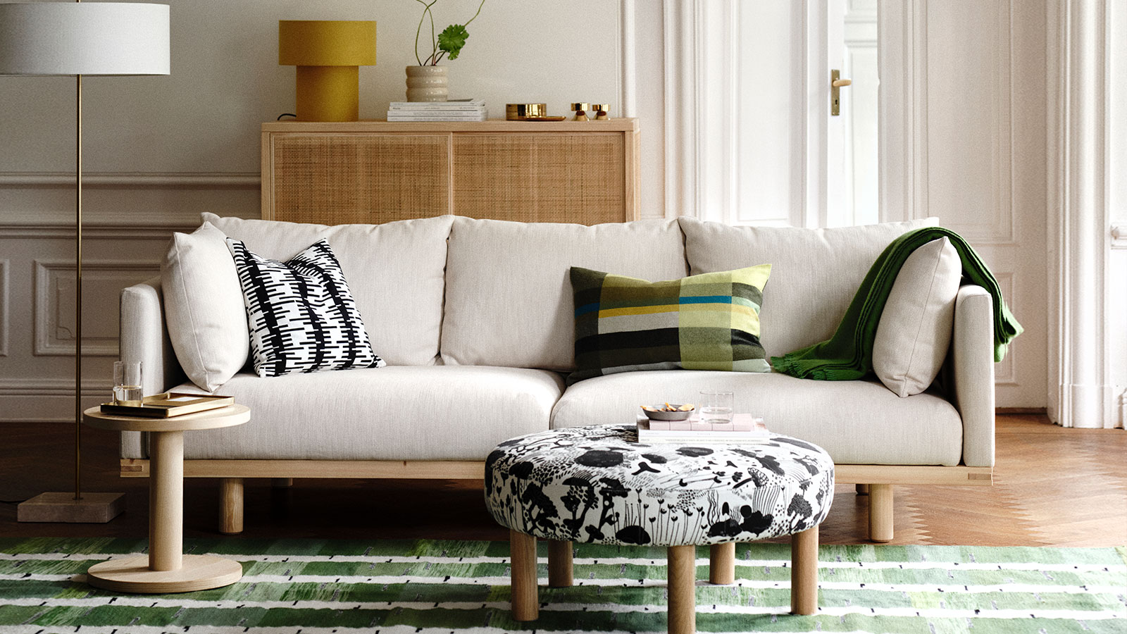 A bright, sunlit living room with a beige STOCKHOLM 2025 three-seat sofa, complemented by decorative cushions.