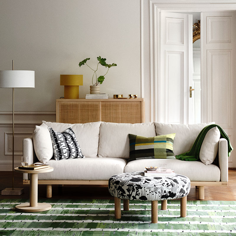 A bright, sunlit living room with a beige STOCKHOLM 2025 three-seat sofa, complemented by decorative cushions.