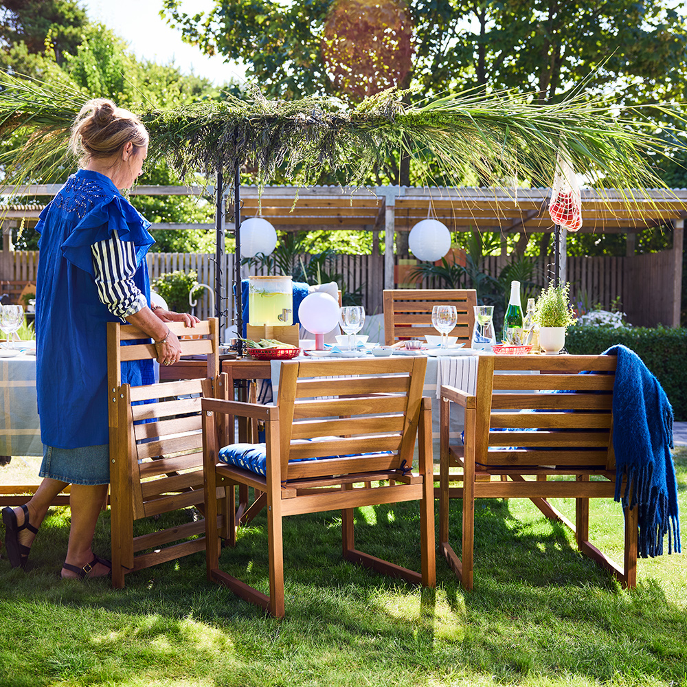 An outdoor dining area features a light brown stained NÄMMARÖ chair with armrests around a wooden table set for a meal.