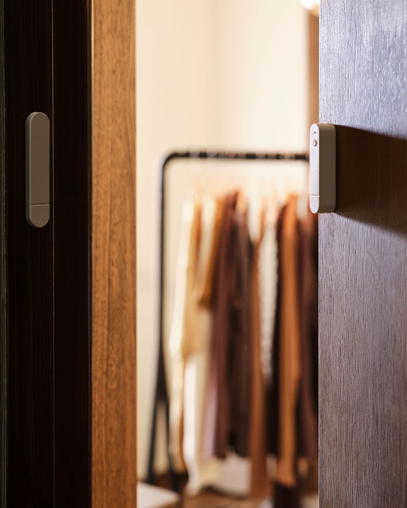 The two parts of a MYGGBETT door/window sensor are mounted on a door and on the door jamb. The door is open.