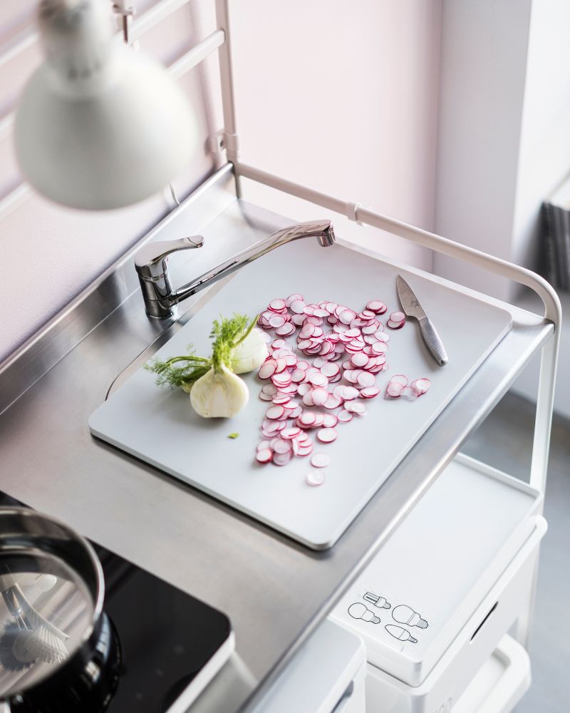 Bright kitchen with TILLREDA stove, IKEA 365+ pan and a KUGGIS box below the counter while slicing vegetables.