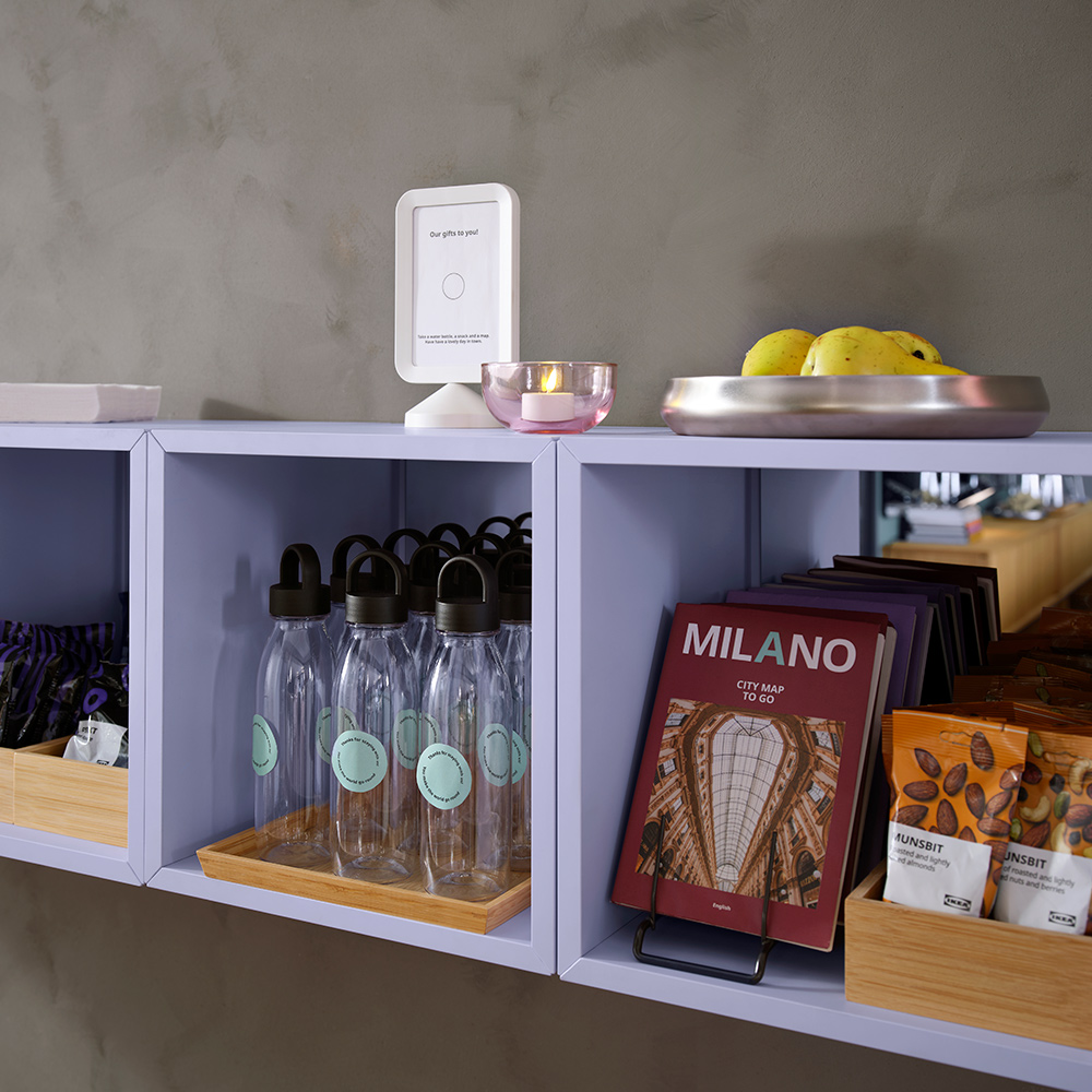 A row of three pale lilac EKET cabinets are mounted on a cement wall. They hold tourist maps, water bottles and snacks.