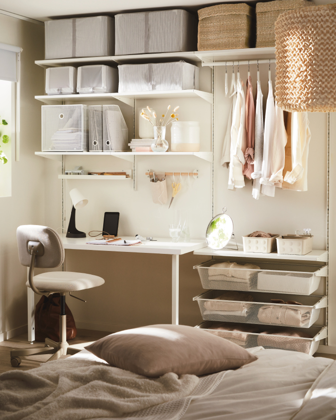 Bedroom space with an open storage system featuring shelves, storage boxes, and hanging clothes, next to a small desk with a lamp and chair.