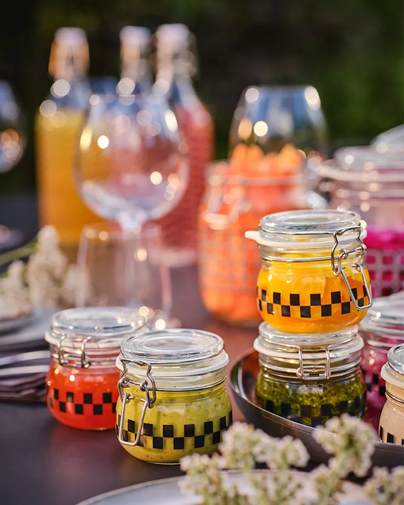 Small glass jars with brightly colored sauces, adorning a festive outdoor table.