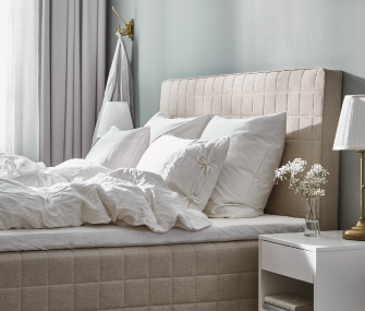 Cama elegante con cabecera tapizada, colchón acolchado y ropa de cama blanca en un dormitorio moderno.
