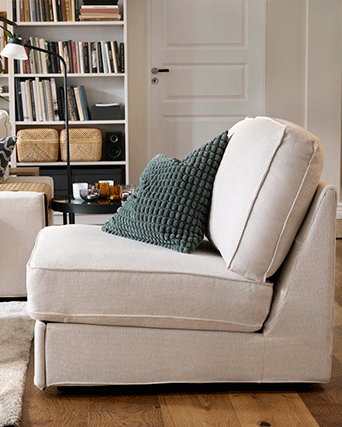 A textured green cushion on a beige armchair in a cozy room with a bookshelf and white door.