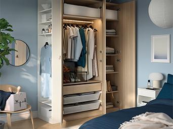 Open wooden wardrobe in a bedroom with organized clothes, drawers, and shelves.