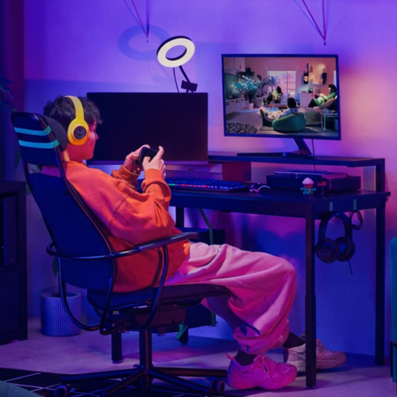 A neon‑lit gaming room with the UTVISNING desk and LÖPARBANA chair, enhanced by the LÅNESPELARE ring light for a vibrant setup.