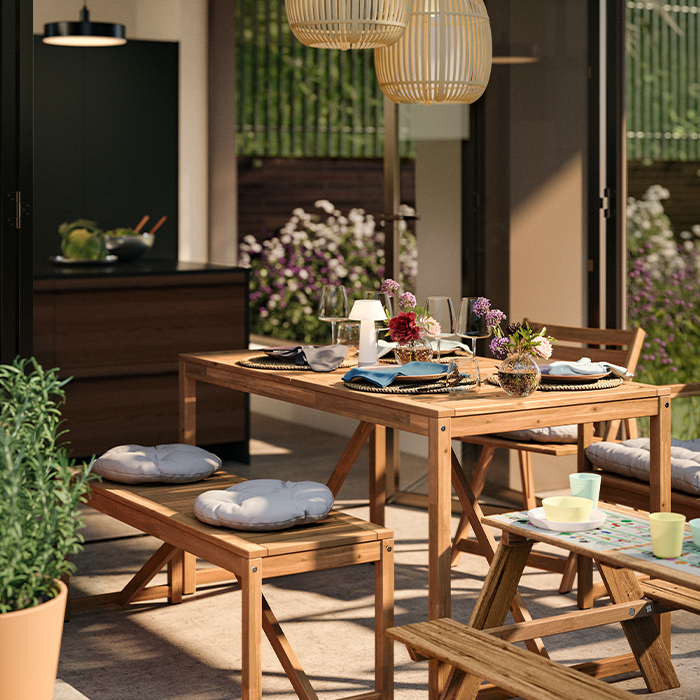 Patio soleado con una mesa de comedor de madera decorada con flores silvestres, cristalería y una vista a una cocina moderna.