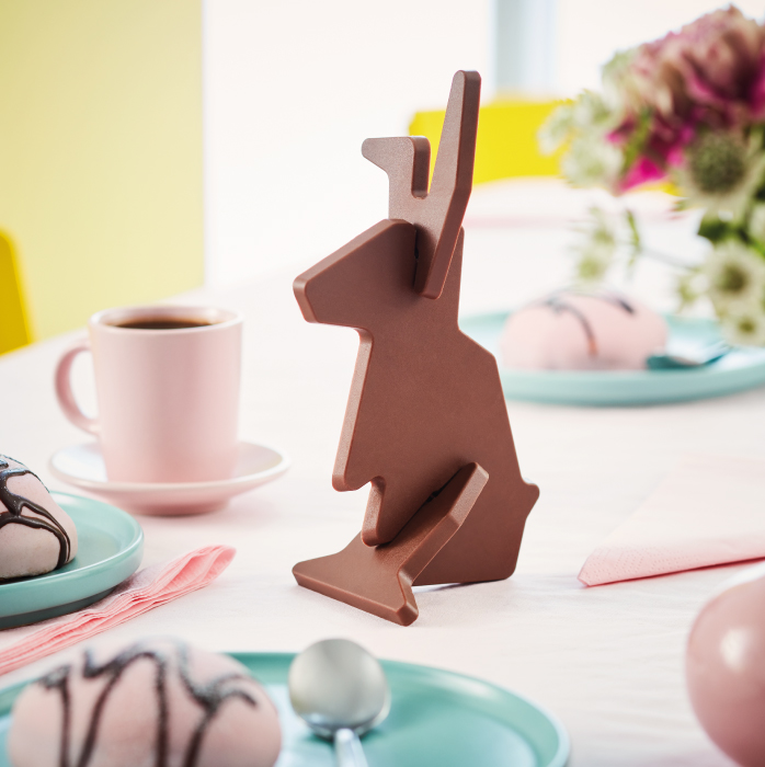 Figura de conejo hecha de chocolate sobre una mesa pastel con café y postres.