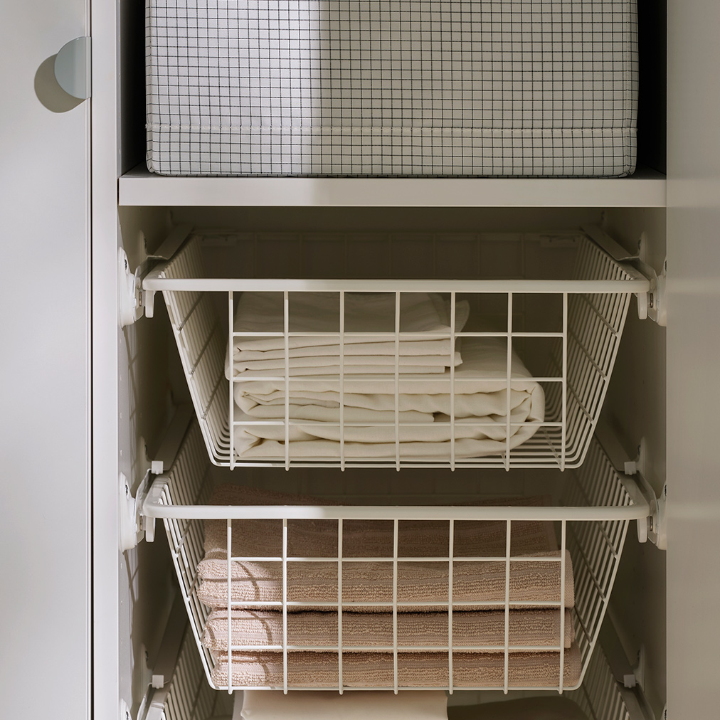 Inside a LASTARE wardrobe combination with STUK boxes on shelves and wire baskets storing neatly folded textiles.
